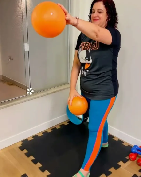 Paciente em pé fazendo exercício com bolas de fisioterapia sobre tatame, em frente ao espelho da sala.